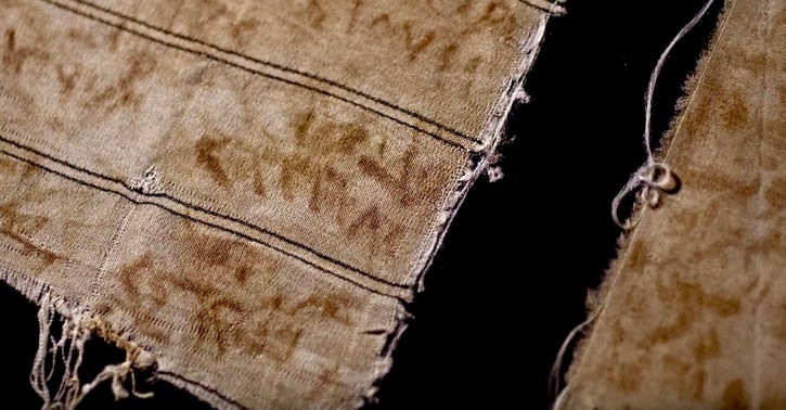 An image of frayed pieces of cloth with faded red names in Arabic script, against a black background.
